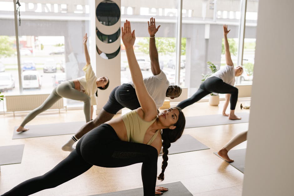 A diverse group of adults practicing yoga poses in a bright, modern studio with large windows.