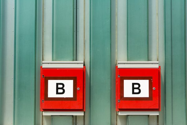 Two red fire alarm boxes labeled 'B' against a green corrugated metal wall.