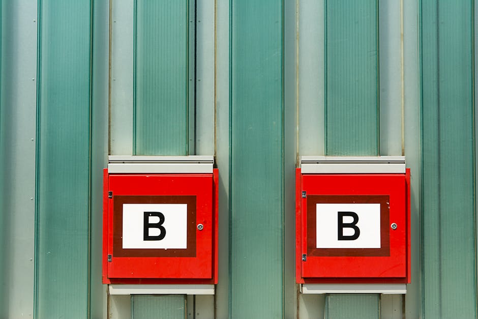 Two red fire alarm boxes labeled 'B' against a green corrugated metal wall.