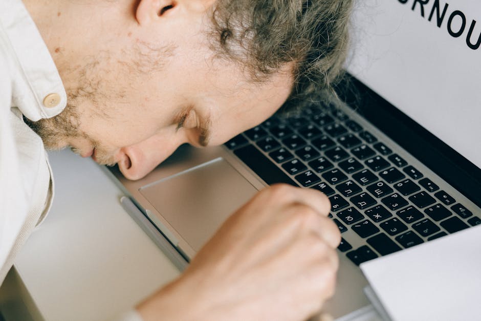 Exhausted employee resting head on laptop keyboard due to burnout and stress.