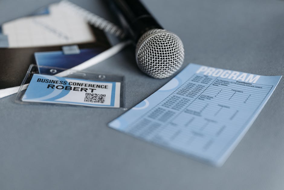 Close-up of a microphone, name tag, and program guide on a table at a business conference.