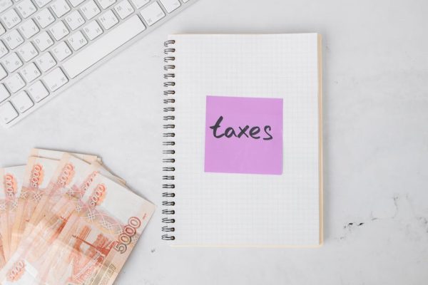 Flat lay image of tax preparation, featuring cash, a notebook, and a computer keyboard on a white surface.