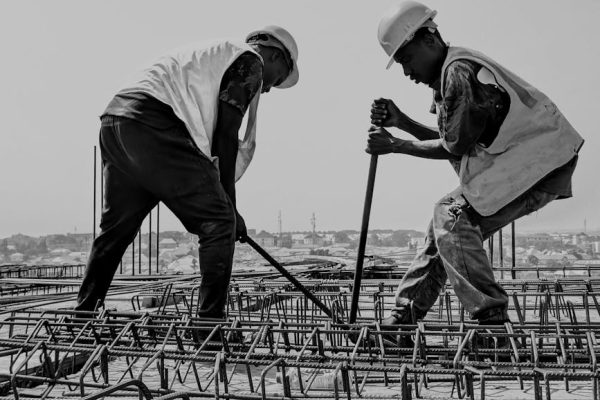 Black and white image of two construction workers reinforcing steel bars on a building site.