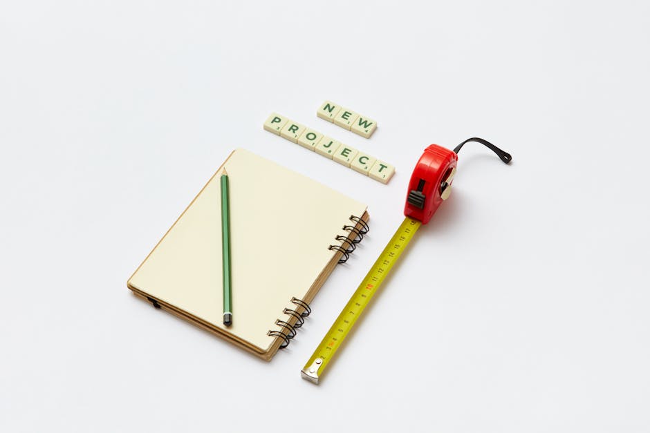 Flat lay of a notebook, pencil, tape measure, and scrabble tiles spelling 'new project'. Ideal for creative work concepts.