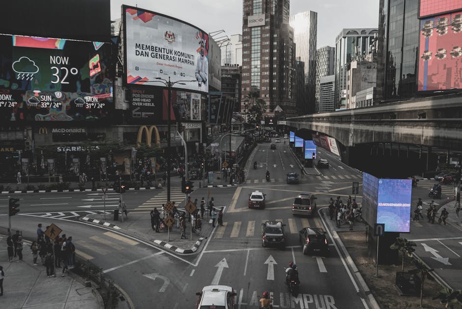 City street view of Kuala Lumpur showcasing traffic and billboards under a cloudy sky.