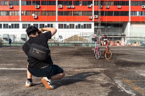 Photographer kneels to capture bicycles against a striking red and white building in Singapore.