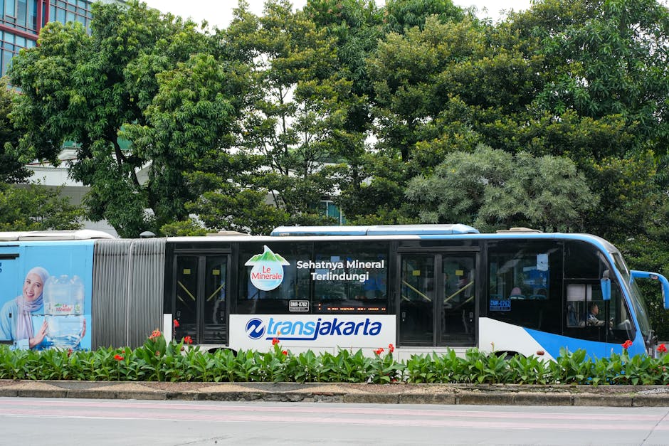 TransJakarta bus passing through a green urban park area with advertisement