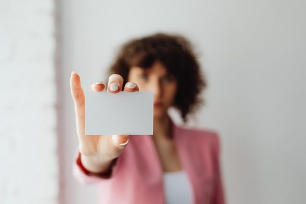 A professional woman in pink suit presenting a blank business card indoors.