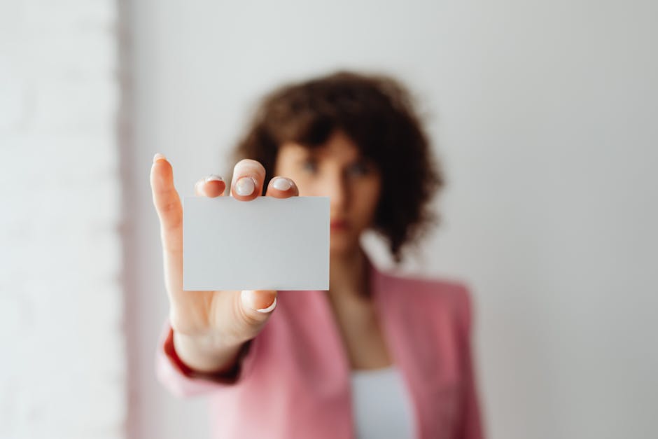 A professional woman in pink suit presenting a blank business card indoors.