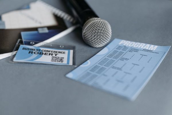 Close-up of a microphone, name tag, and program guide on a table at a business conference.