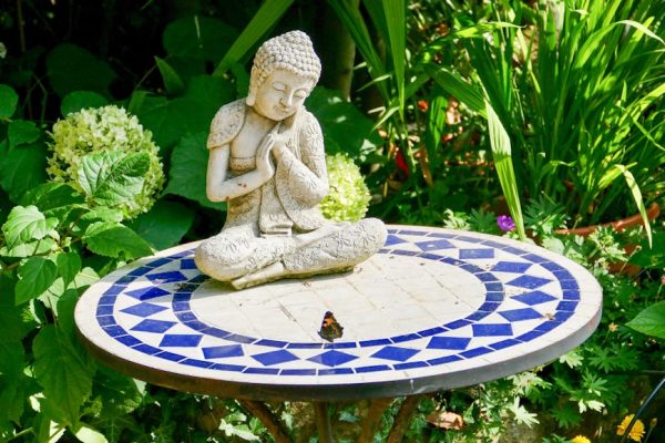 A serene Buddha statue on a mosaic table surrounded by lush greenery in an English garden.