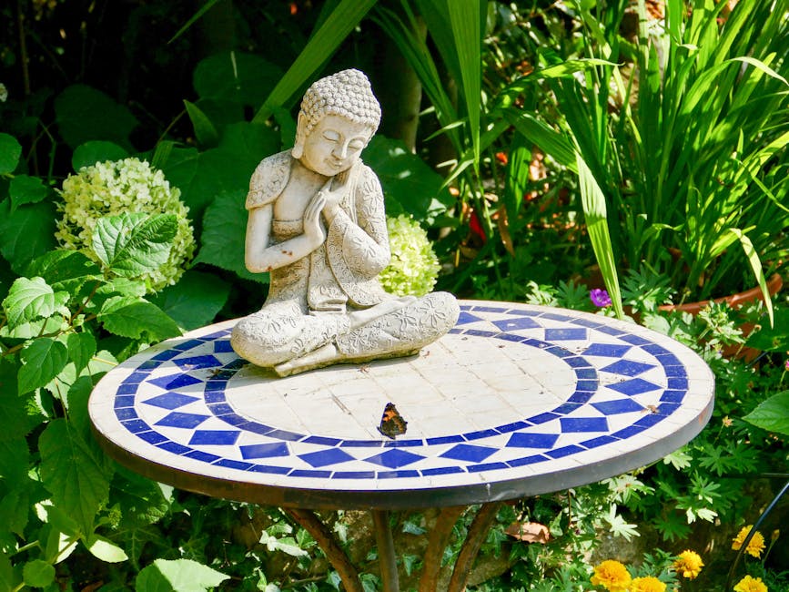 A serene Buddha statue on a mosaic table surrounded by lush greenery in an English garden.