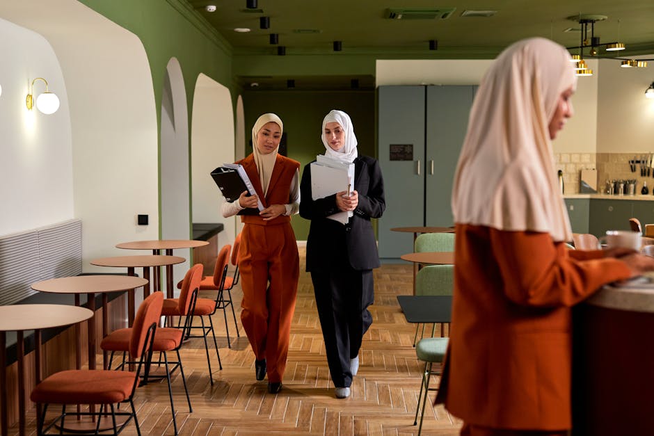 Professional businesswomen in hijabs walk through a modern office space, depicting diversity and teamwork.
