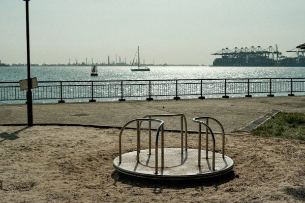 Carousel and sandy playground by Singapore's harbor, with industrial views.