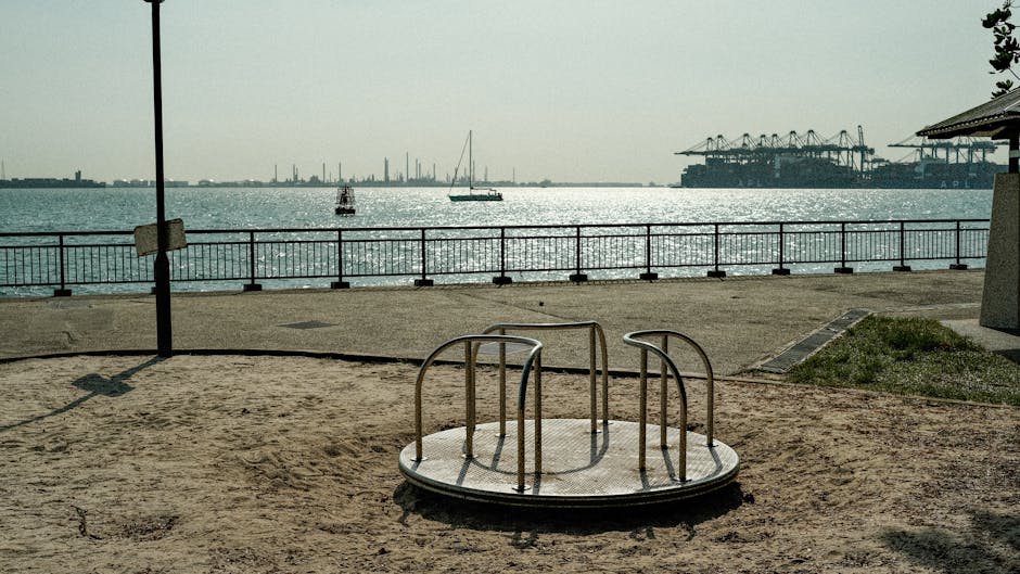 Carousel and sandy playground by Singapore's harbor, with industrial views.