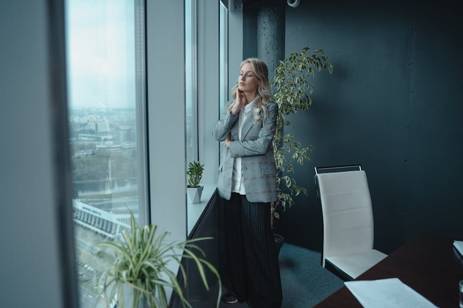 Businesswoman in modern office looking out of window, deep in thought.