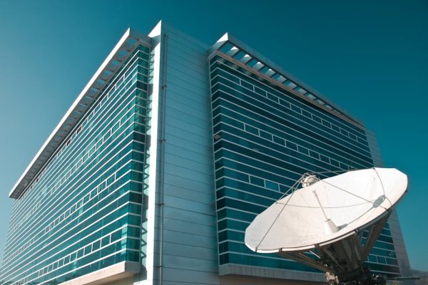A striking modern glass building in Santiago, Chile, featuring a large satellite dish under a clear blue sky.