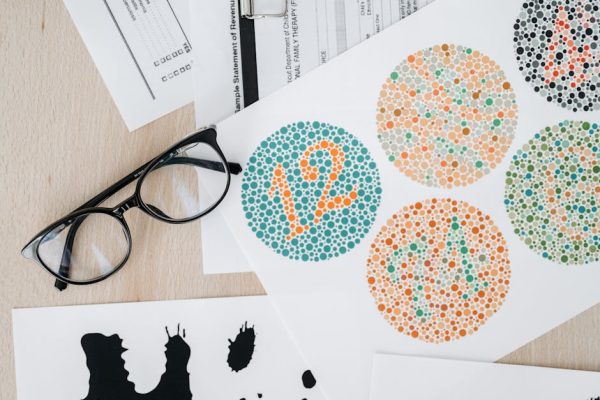 Close-up of color blindness test sheets with eyeglasses on a wooden table.