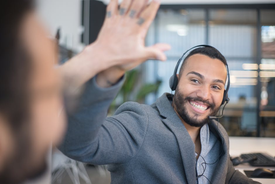 A cheerful call center agent with a headset gives a high five to a colleague in an office.