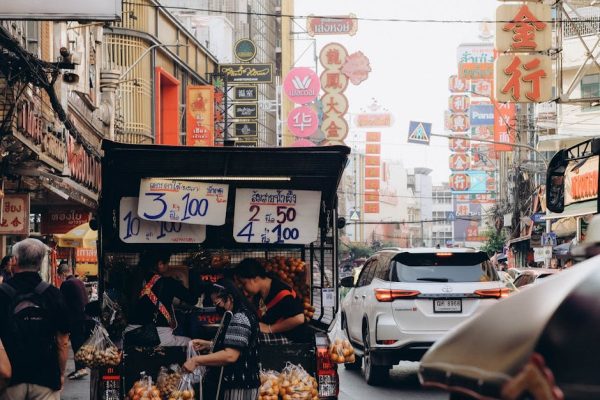 Vibrant street market with colorful signs in Bangkok, bustling with people and cars.