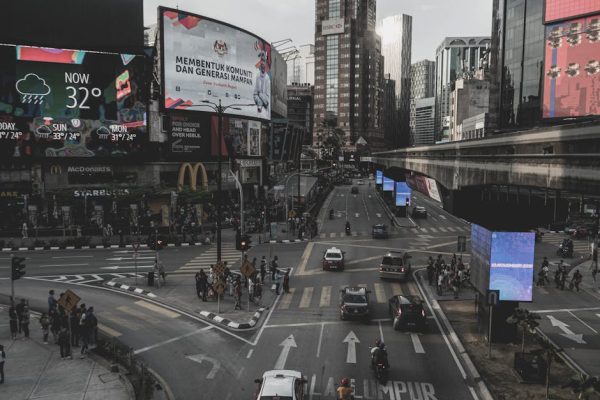 City street view of Kuala Lumpur showcasing traffic and billboards under a cloudy sky.