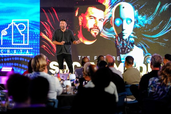 Man presents on stage with robot graphic background