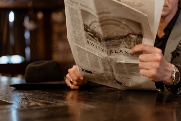 Close-up of man reading newspaper with focus on Switzerland headline.