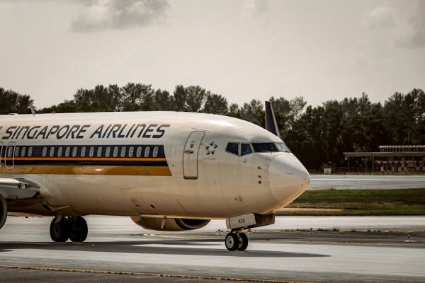 Singapore Airlines plane taxiing on airport runway under cloudy skies.