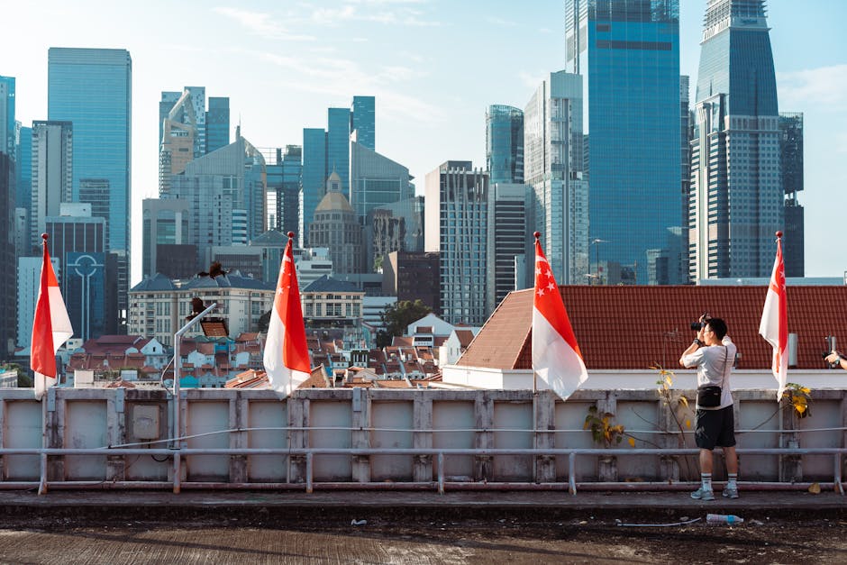 A photographer takes a picture of the Singapore skyline under a clear blue sky.