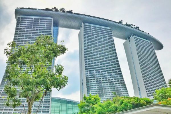 From below exterior of modern stylish skyscrapers complex surrounded with lush green trees against cloudy sky in Singapore