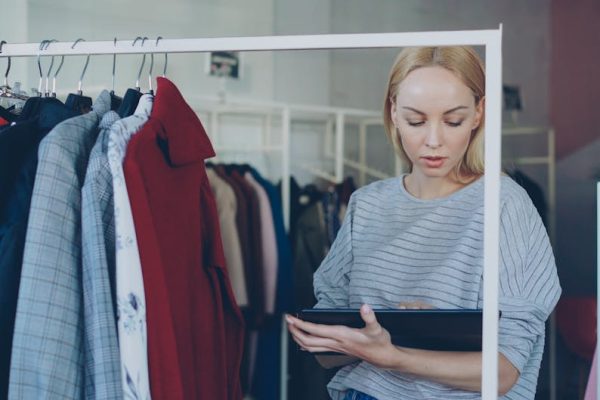 Female retail employee using a tablet for inventory management in a clothing store.