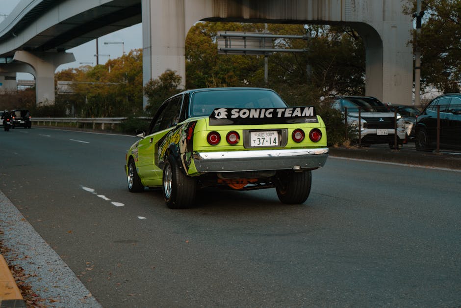 A vintage green car drives on an urban highway in Tokyo with distinct banners and decals.