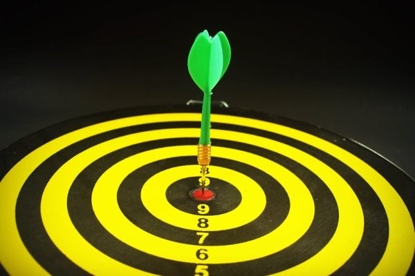 Close-up of a green dart hitting the bullseye on a yellow and black target board, symbolizing precision and success.