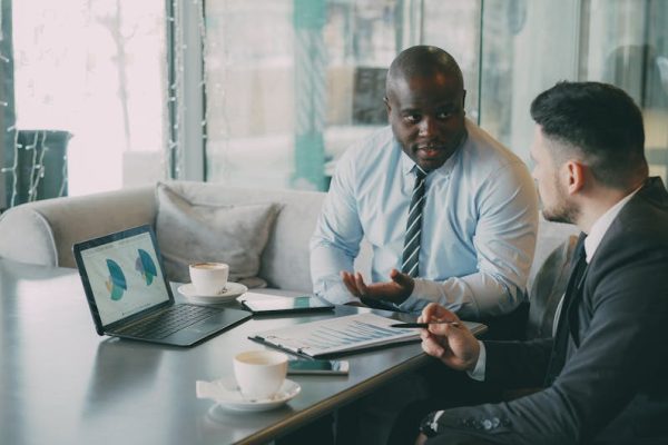 Two business professionals engaged in discussion over laptops and documents.