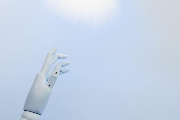 A robotic hand reaching towards a bright light on a white background symbolizing innovation.