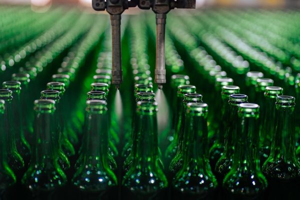 Rows of green glass bottles on an automated production line in a factory setting.
