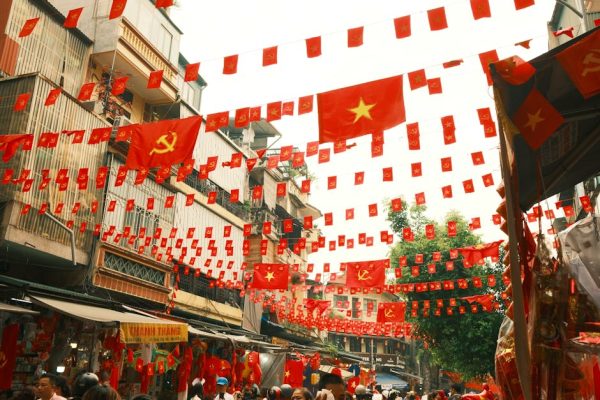 A bustling market street in Vietnam adorned with Vietnamese flags and communist symbols, creating a vibrant atmosphere.