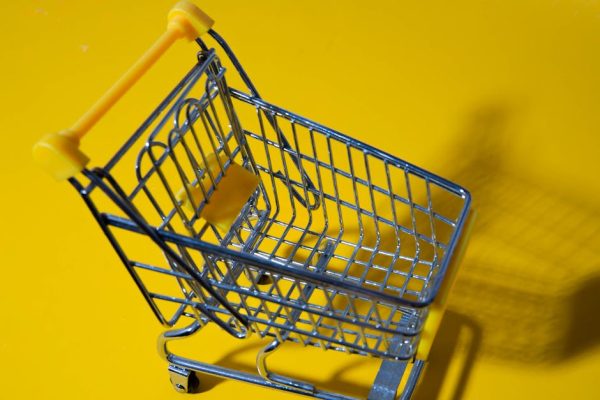 Close-up of a small toy shopping cart on a vibrant yellow backdrop.