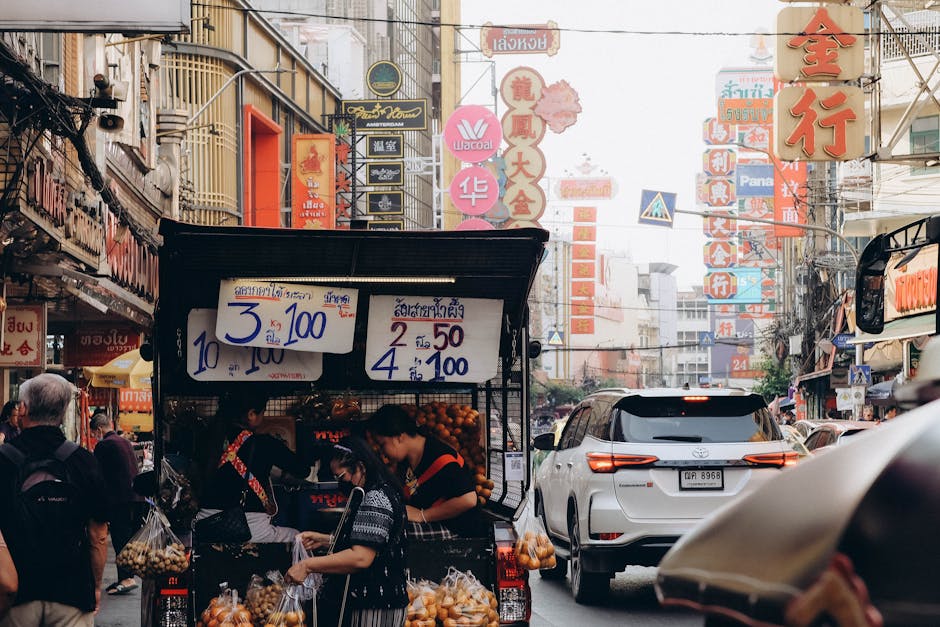 Vibrant street market with colorful signs in Bangkok, bustling with people and cars.