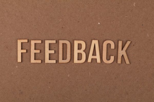 A close-up of a wooden 'FEEDBACK' sign on a textured cardboard background.