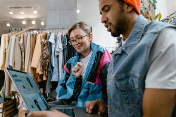 Young professionals discussing online sales strategies at a fashion store using a laptop.