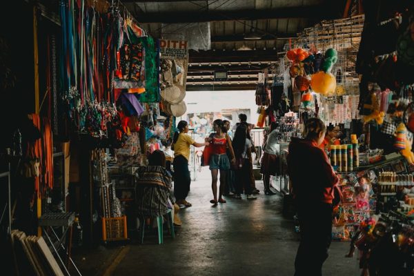 Vibrant indoor market scene with shoppers exploring diverse stalls filled with colorful merchandise.