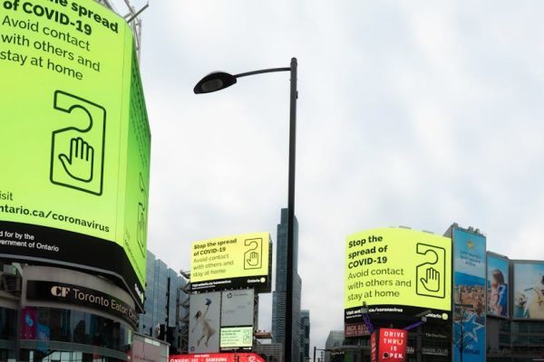 From below of modern buildings with billboards about coronavirus located on on city street under cloudy sky
