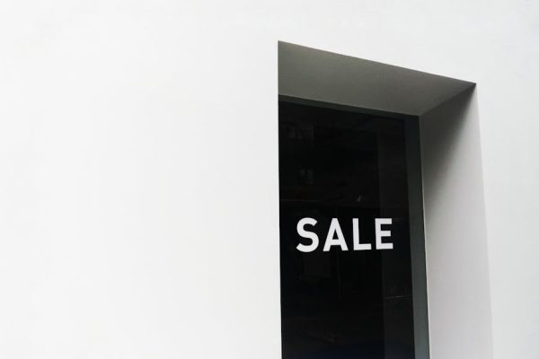 A minimalist black and white image of a sale sign on a store window with ample negative space.