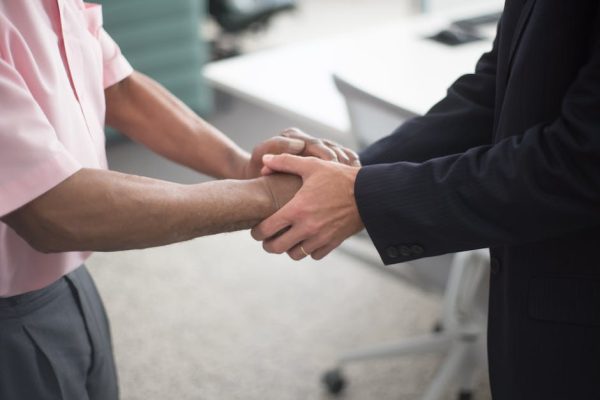 Close-up of a formal handshake between two businessmen in an office environment.