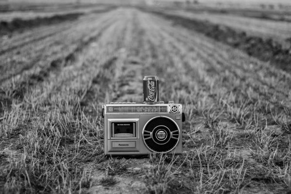 Black-and-white photo of a vintage radio with Coca-Cola can in a field.