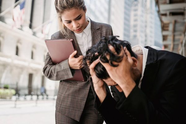 A woman comforts a distressed man in a business environment outdoors.