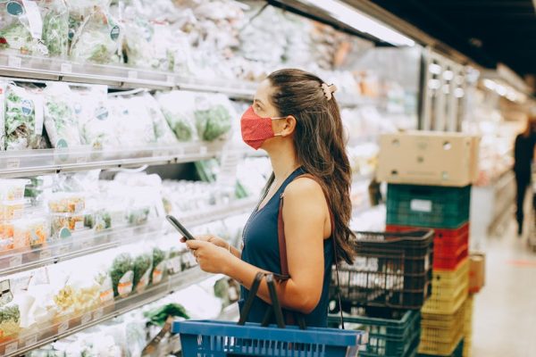 Woman with mask shopping in a grocery aisle, examining fresh produce selection.