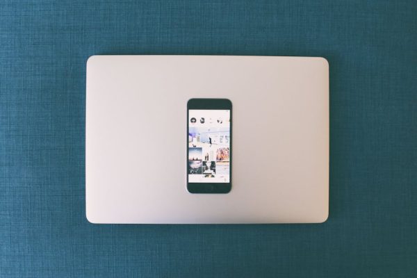 Flat lay of a smartphone on a laptop with social media photos on screen.