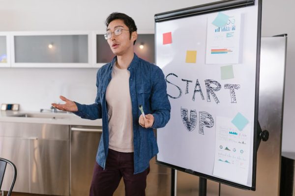 Asian businessman presenting a startup idea with charts and graphs on a whiteboard.